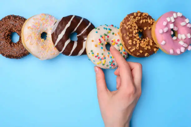 Photo of Sweet tooth creative concept. Top above flatlay close up view photo of woman hand taking yummy tasty round donut isolated over blue pastel background