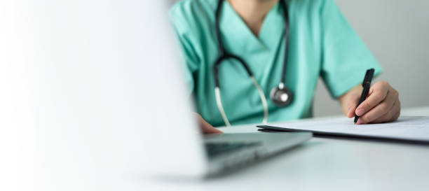 asian female nurse or surgeon doctor in green uniform working on laptop and writing something information of patient in paperwork checklist. - white green colors paper imagens e fotografias de stock