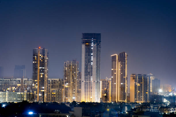 High rise multi story skyscrapers lit up at night with small houses in the foreground at night in gurgaon delhi High rise multi story skyscrapers lit up at night with small houses in the foreground at night in gurgaon delhi. Shows the rapid pace of development of the real estate sector with property, offices and residences on a pollution free clear day delhi photos stock pictures, royalty-free photos & images