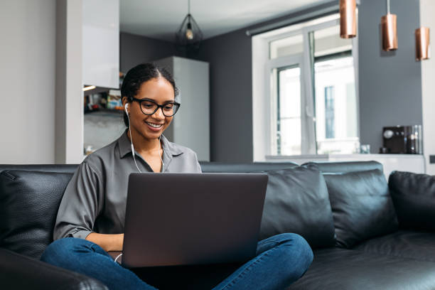 videochiami di giovani donne che usano un laptop seduto su un divano che indossa auricolari - executive apartment foto e immagini stock