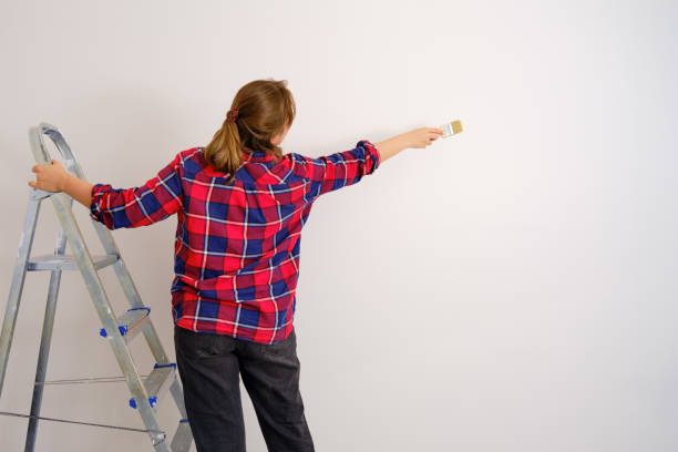 istock Painter in a plaid shirt paints the wall with white paint, copy space 1219718676