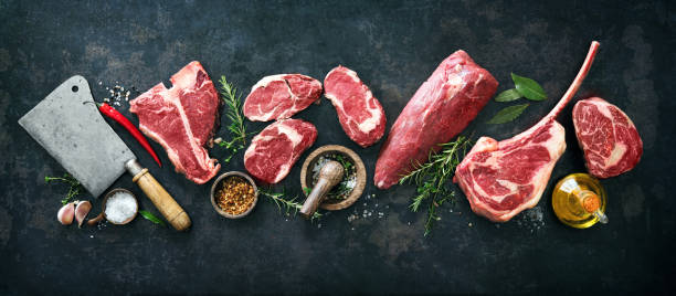 vielzahl von rohen rindfleisch-fleischsteaks zum grillen mit gewürzen und utensilien - fleisch stock-fotos und bilder
