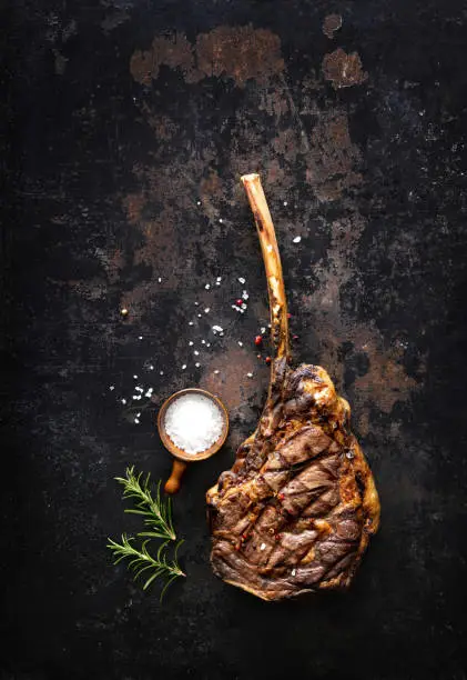 Grilled tomahawk beef steak with spices on dark rustic background