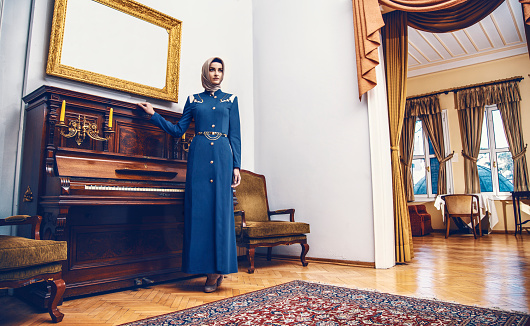 Modern young muslim woman standing near of old piano and looking away