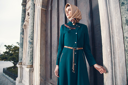 Beautiful muslim woman standing in front of caravanserai gate. She is looking away