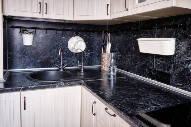 istock A corner with a sink in a white kitchen with a black marble countertop with a railing. Colander, sockets, knives, bottle and cutlery above the table 1219723598