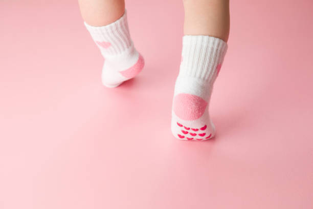 Baby going on light pink floor background. Pastel color. Feet in anti slip socks. Infant first steps. Closeup. Back view. Baby going on light pink floor background. Pastel color. Feet in anti slip socks. Infant first steps. Closeup. Back view. babyhood photos stock pictures, royalty-free photos & images