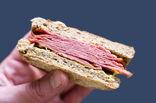 Sliced pastrami meat in a bun sandwich with mustard.