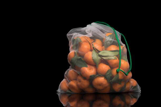 Tangerines in a reusable mesh bag. Isolated black background with copy space. Christmas and New Year food in zero waste concept. The use of reusable bags is good for the environment.