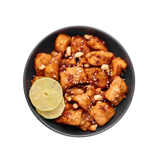 Photo of Korean Sweet Fried Chicken Dakgangjeong in black bowl isolated on white background. Dakgangjeong is korean cuisine dish with deep fried crunchy chicken in sweet sauce. Korean Food