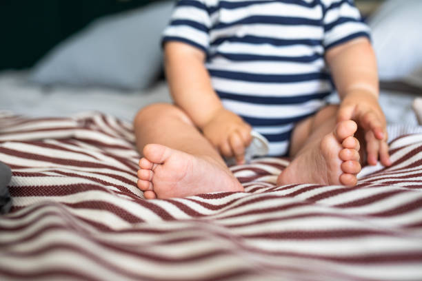 Tiny feet of a baby boy in a striped suit sitting on a bed.
