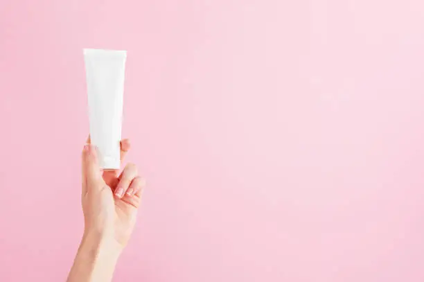 Unbranded flacon for cream, concealer, toiletry. Plastic tube in female hand. Container for professional cosmetics products. Skincare and beauty concept. Mockup, copy space. Isolated on pink.