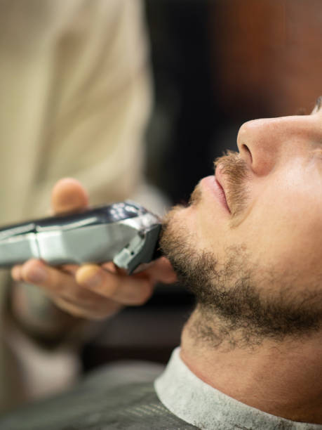 istock Barber using electric razor while trimming a beard of male customer 1219731892