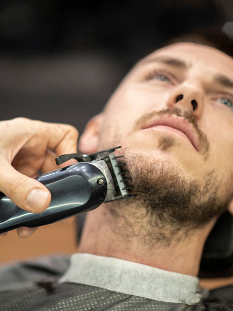 istock Barber using electric razor while trimming a beard of male customer 1219731902