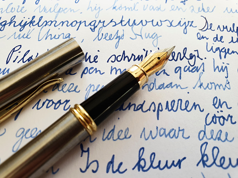 Close-up of blue ink handwriting with fountain pen on paper, correspondence and communication photograph, selective focus on the nib of the pen.