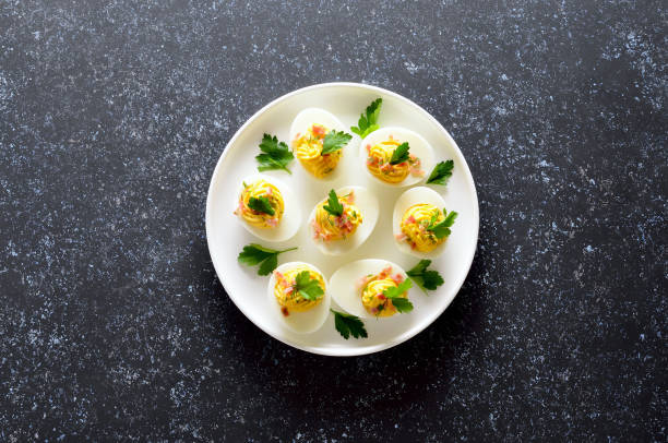 istock Stuffed eggs with egg yolk, bacon, mustard and parsley on dark stone background 1219735569