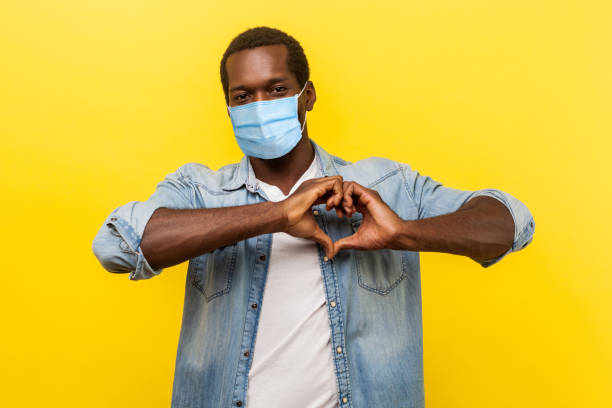 Romantic relations. Portrait of handsome cheerful man with surgical medical mask making heart shape with hands, expressing love feelings or friendship. Romantic relations. Portrait of handsome cheerful man with surgical medical mask making heart shape with hands, expressing love feelings or friendship. indoor studio shot isolated on yellow background peace sign gesture photos stock pictures, royalty-free photos & images