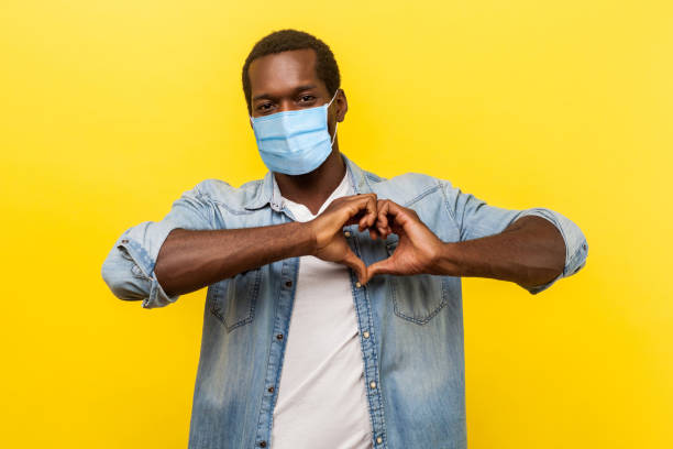 romantic relations. portrait of handsome cheerful man with surgical medical mask making heart shape with hands, expressing love feelings or friendship. - made man object imagens e fotografias de stock