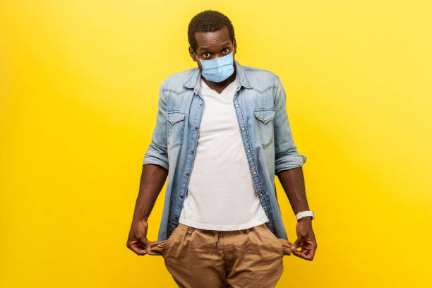 No money or fired work. Portrait of frustrated stressed poor man with surgical medical mask showing empty pockets inside out, going bankrupt, no cash for living No money or fired work. Portrait of frustrated stressed poor man with surgical medical mask showing empty pockets inside out, going bankrupt, no cash for living. indoor, isolated on yellow background over spend stock pictures, royalty-free photos & images