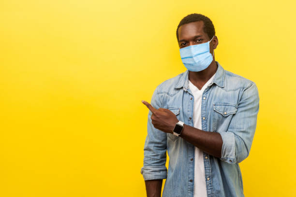 look, advertise here! portrait of positive man with surgical medical mask pointing left side and smiling at camera, showing empty space for advertise. - aside imagens e fotografias de stock