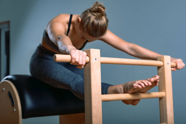 Beautiful positive blond woman is being prepared performing pilates exercise, training on barrel equipment. Fitness concept, special fitness equipment, healthy lifestyle, plastic. Copy space, sport banner for advertising hermosa mujer rubia positiva está siendo preparada realizando ejercicio de pilates, entrenamiento en equipos de barril. concepto de fitness, equipo de fitness especial, estilo de vida saludable, plástico. copiar espacio, banner deportivo para publicidad