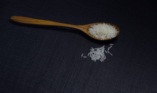 istock Wood spoon and raw rice on black canvas background 1219744262