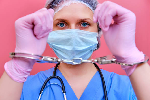 A nurse on a pink background shows hands in handcuffs, closeup. Doctor arrested for a bribe from a patient, concept A nurse on a pink background shows hands in handcuffs, closeup. Doctor arrested for a bribe from a patient, concept arrest photos stock pictures, royalty-free photos & images