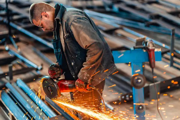 Manual worker using grinding machine in steel factory.