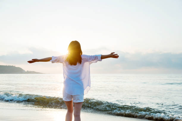 istock Young woman standing on beach with arms outstretched 1219748803