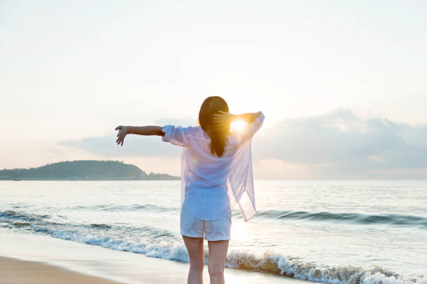 istock Young woman standing on beach with arms outstretched 1219749541