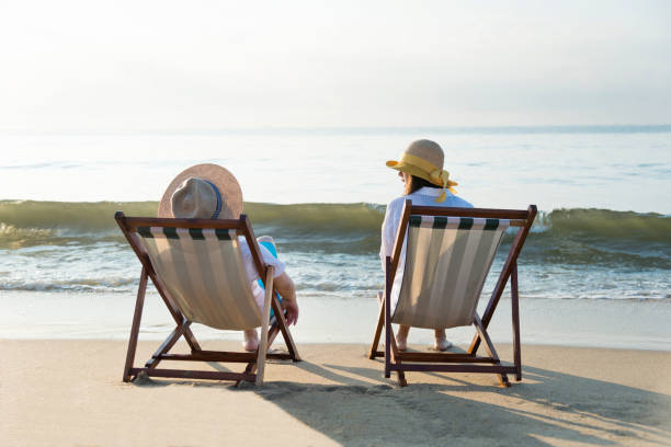 istock Couple sitting on deck chair at beach 1219750998
