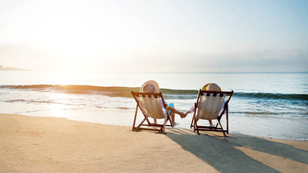 istock Couple sitting on deck chair at beach 1219751024