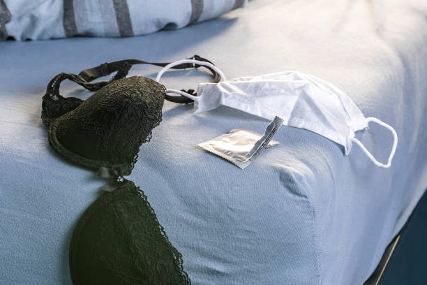Black bra, white medical mask and condom wrapper on the edge of the bed. Sex during quarantine concept. stock photo