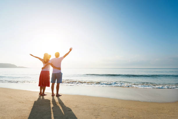 istock Couple standing on the beach with arms raised 1219752227