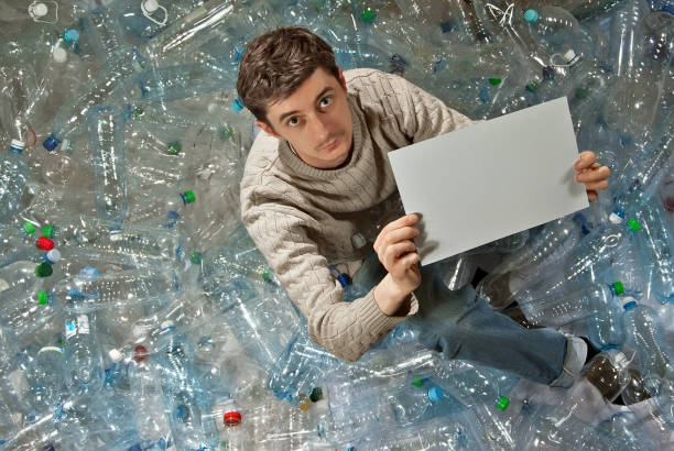 istock Man on the background of empty plastic bottles. Environmental protection concept and plastic pollution. White paper in hands. Place for text. Mockup for design. Copy space for advertising. 1219753805