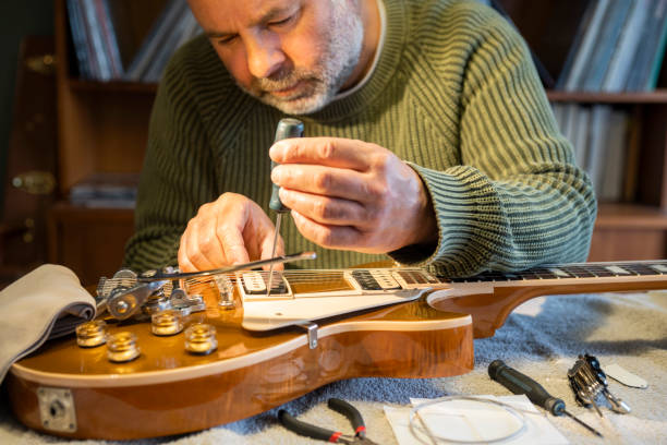 A man working on an electric guitar at home.  He is adjusting components to improve its sound and action.