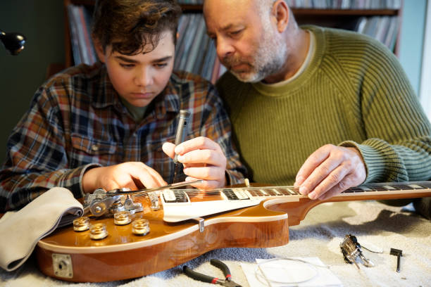 A father teaching his son how to adjust an electric guitar at home A man and his son working on an electric guitar at home.  He is adjusting components to improve its sound and action. father and son guitar stock pictures, royalty-free photos & images