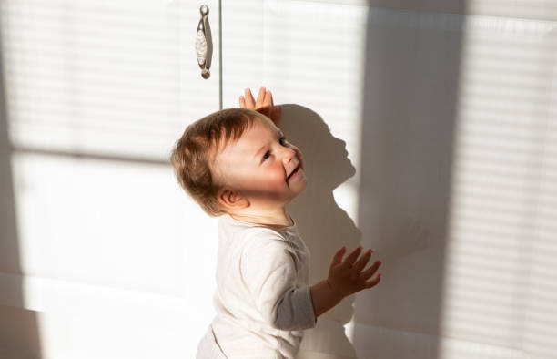 istock Joyful baby making first steps balancing with hands on the white kitchen background with the morning sun falling on him 1219764918