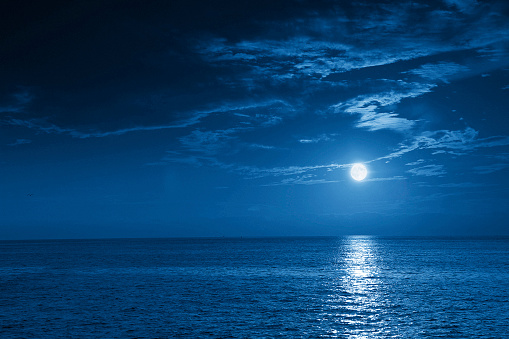 This photo illustration of a deep blue moonlit ocean at night with calm waves would make a great travel background for any coastal region or vacation, emphasizing the beauty of the night time ocean or sea.