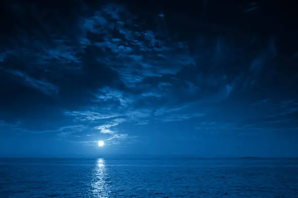 This photo illustration of a deep blue moonlit ocean at night with calm waves would make a great travel background for any coastal region or vacation, emphasizing the beauty of the night time ocean or sea.