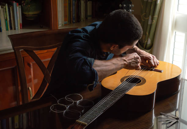 istock Young man changing guitar strings at home near to a bright window. Repairing a classical guitar on wooden table with new strings and tools. 1219769621