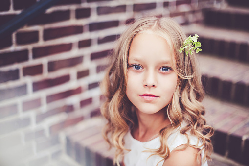 Authentic portrait of beautiful 9-10 years old girl with blond curly hair sitting on the stairs. Outdoor fashion preteen photoshot.