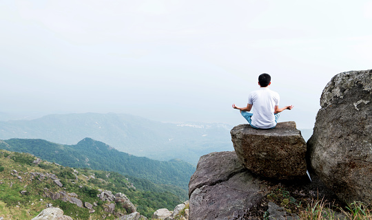 Man doing yoga on top of mountain.