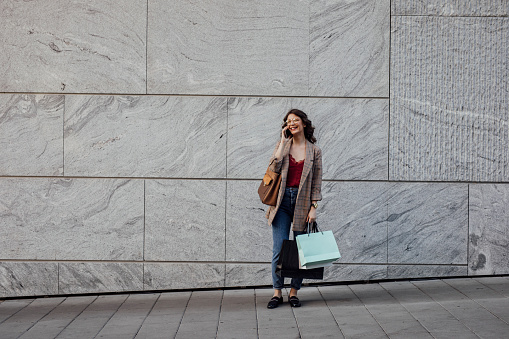 Smiling woman with shopping bags talking on the phone outdoors.