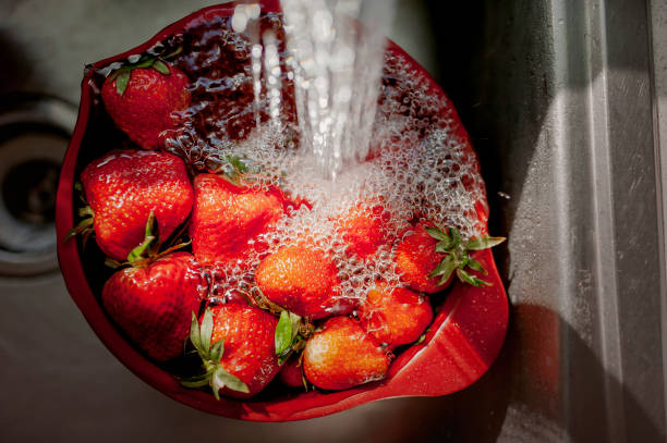 schale erdbeeren unter fließendem wasser in einer küchenspüle - washing fruit preparing food strawberry stock-fotos und bilder