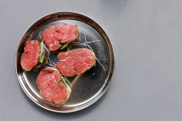 Four prepared tenderloin steaks ready for barbecue on silver plate on grey surfaced table