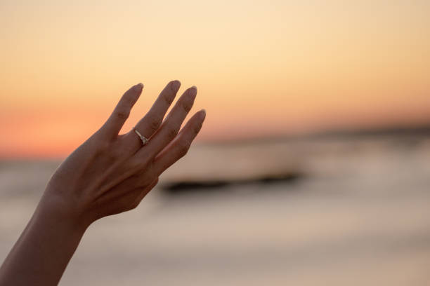 istock Womans hand with engagement ring held against sunset 1219779505