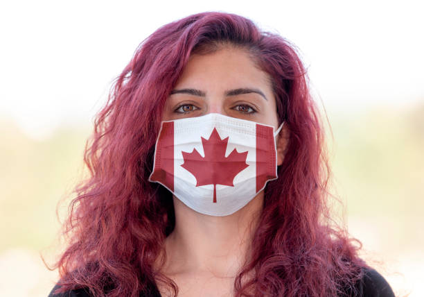 A portrait of a young woman wearing a face mask with Canadiam flag design because of new coronavirus (Covid-19) pandemic. Taken via medium format camera. Flag made in Adobe Illustrator CC