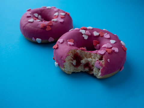 Bitten donut with berry filling on blue background. Two pink glazed donuts decorated with hearts.