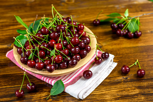 Fresh sour cherries in a wooden bowl, cloth and green leaves on the board. Fresh ripe sour cherries.